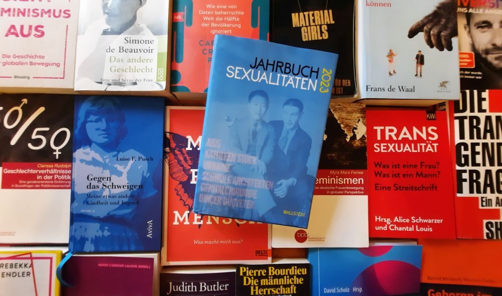Jahrbuch Sexualitäten 2023 liegt auf einen Bücherteppich anderer Bücher zu LGBTQIA und Feminismus mit unerschiedlichen Positionen