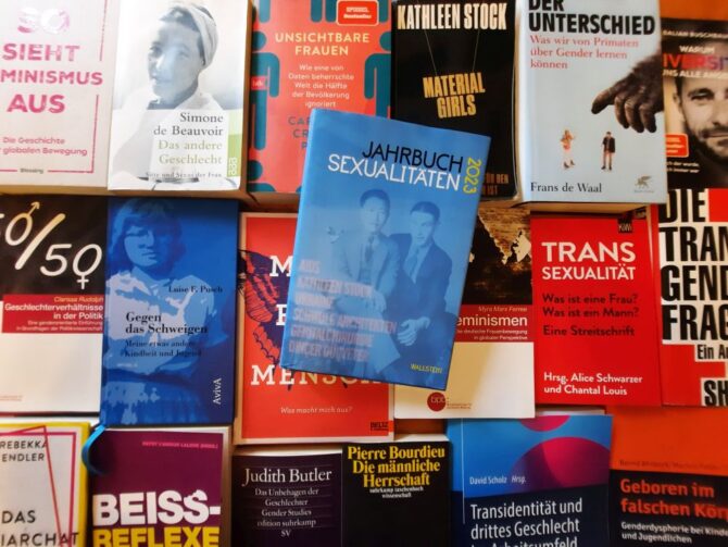 Jahrbuch Sexualitäten 2023 liegt auf einen Bücherteppich anderer Bücher zu LGBTQIA und Feminismus mit unerschiedlichen Positionen